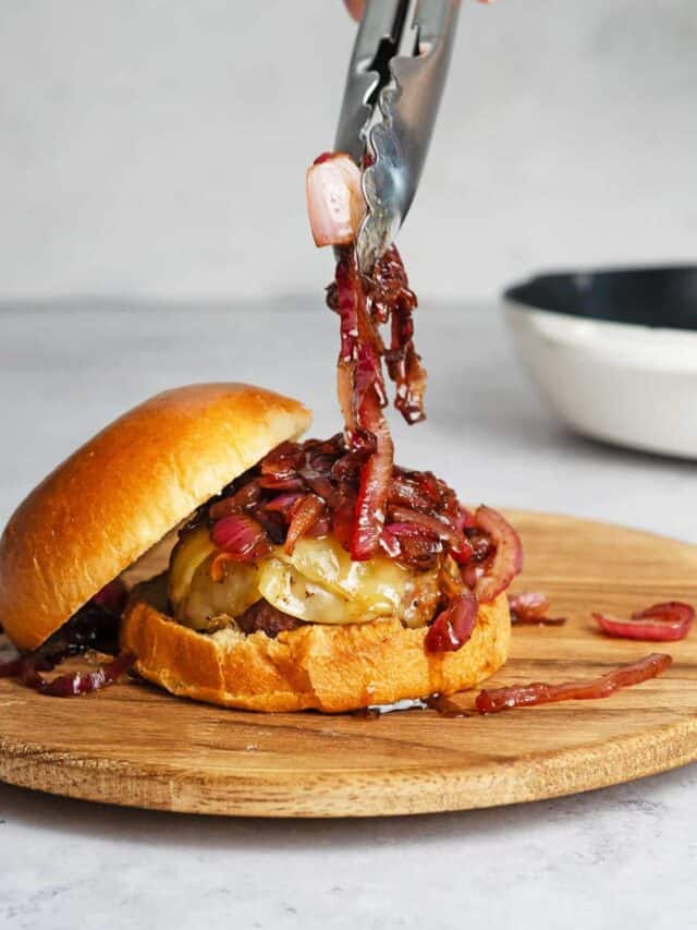 using tongs to place caramelized onions on a burger