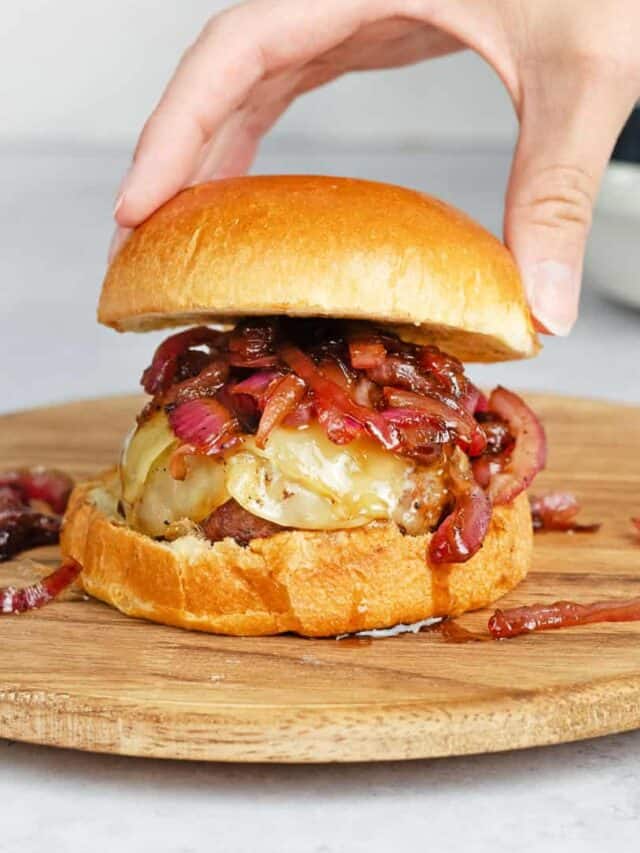 placing a bun on top of a burger with caramelized onions
