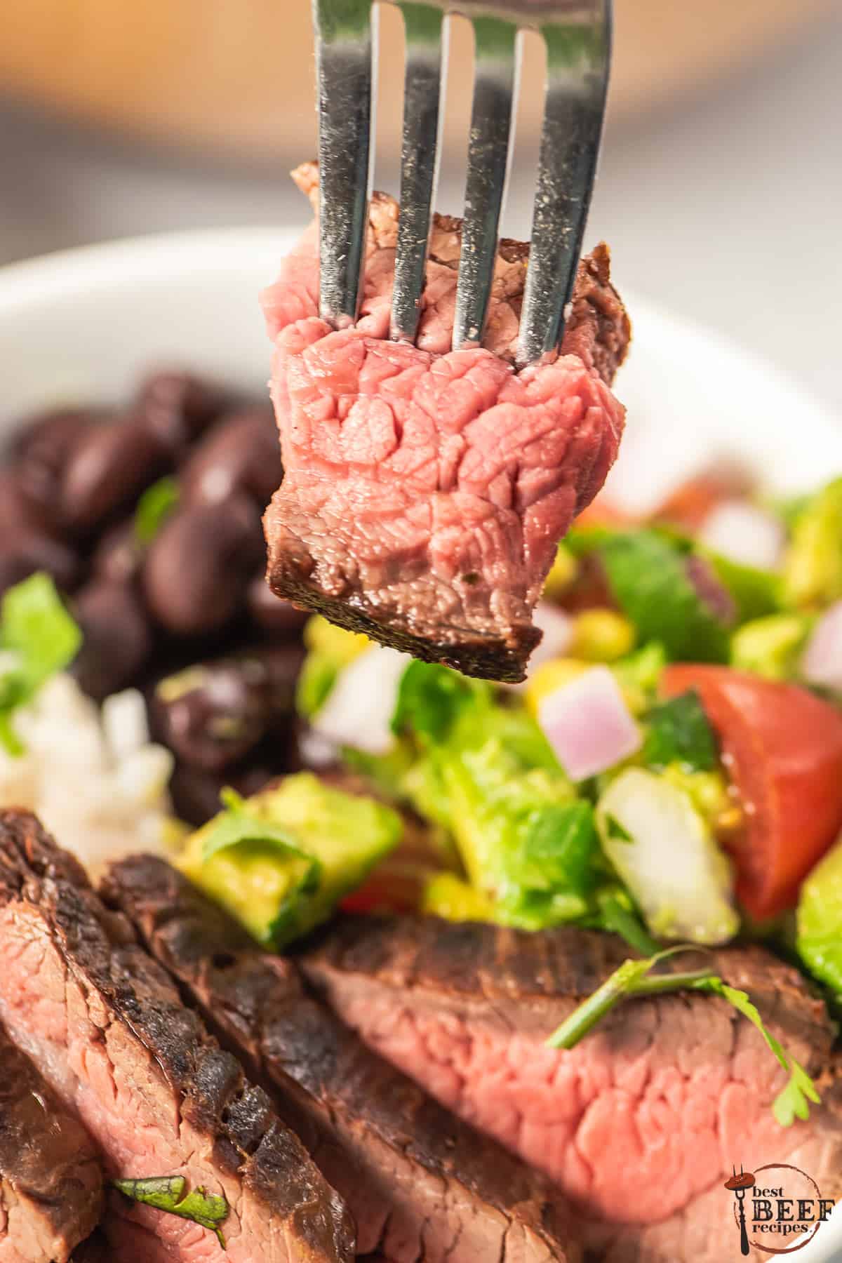 a closeup of a fork taking away a slice of tender guajillo steak