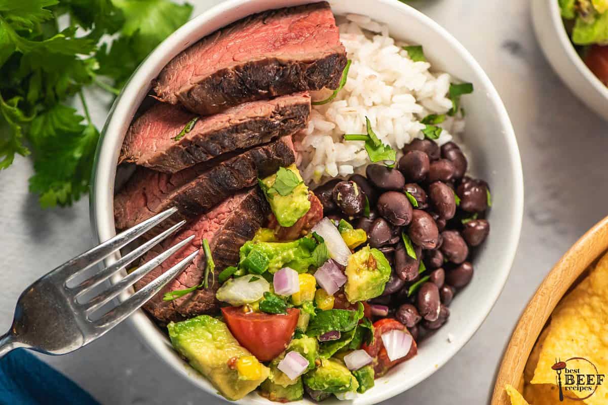 a bowl of guajillo steak with black beans, avocado salsa, and rice