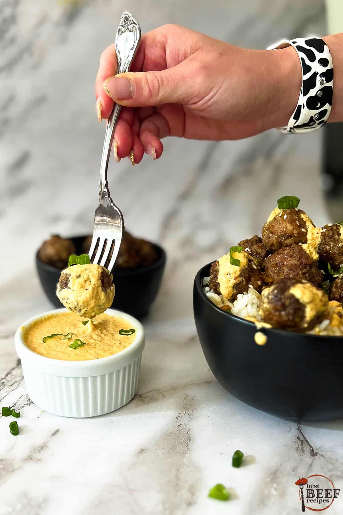 a hand dipping a meatball on a fork into sauce