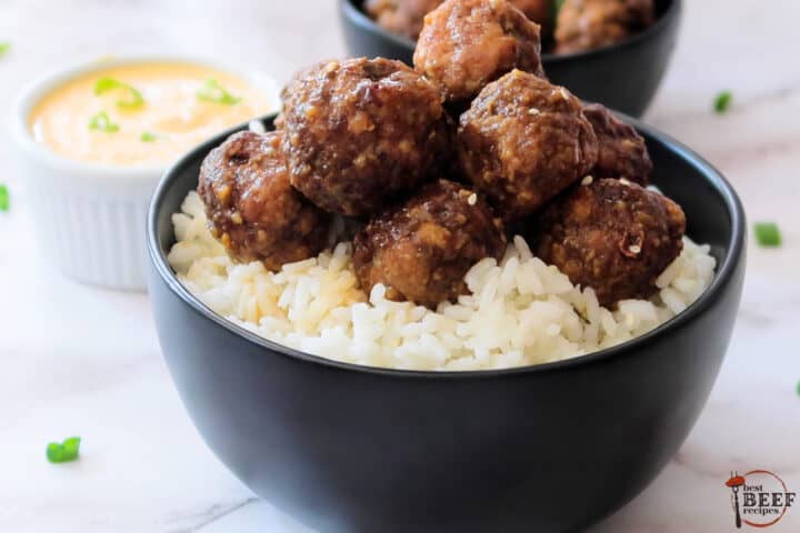 a black bowl filled with rice and completed korean meatballs with dip in the background