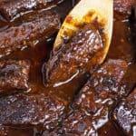 a wooden spoon scooping short ribs out of a bath of marinade