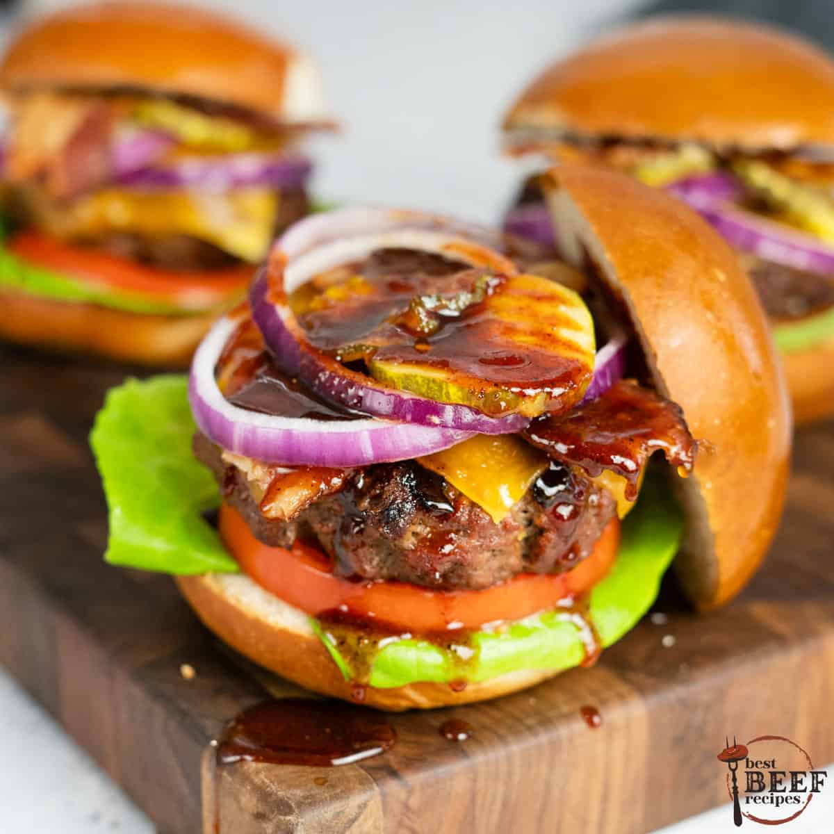 3 bbq burgers on a serving board, close up with one dripping with bbq sauce