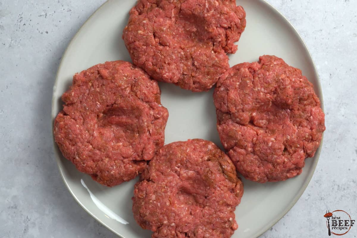four burger patties on a white plate with thumbprints in the middle of each