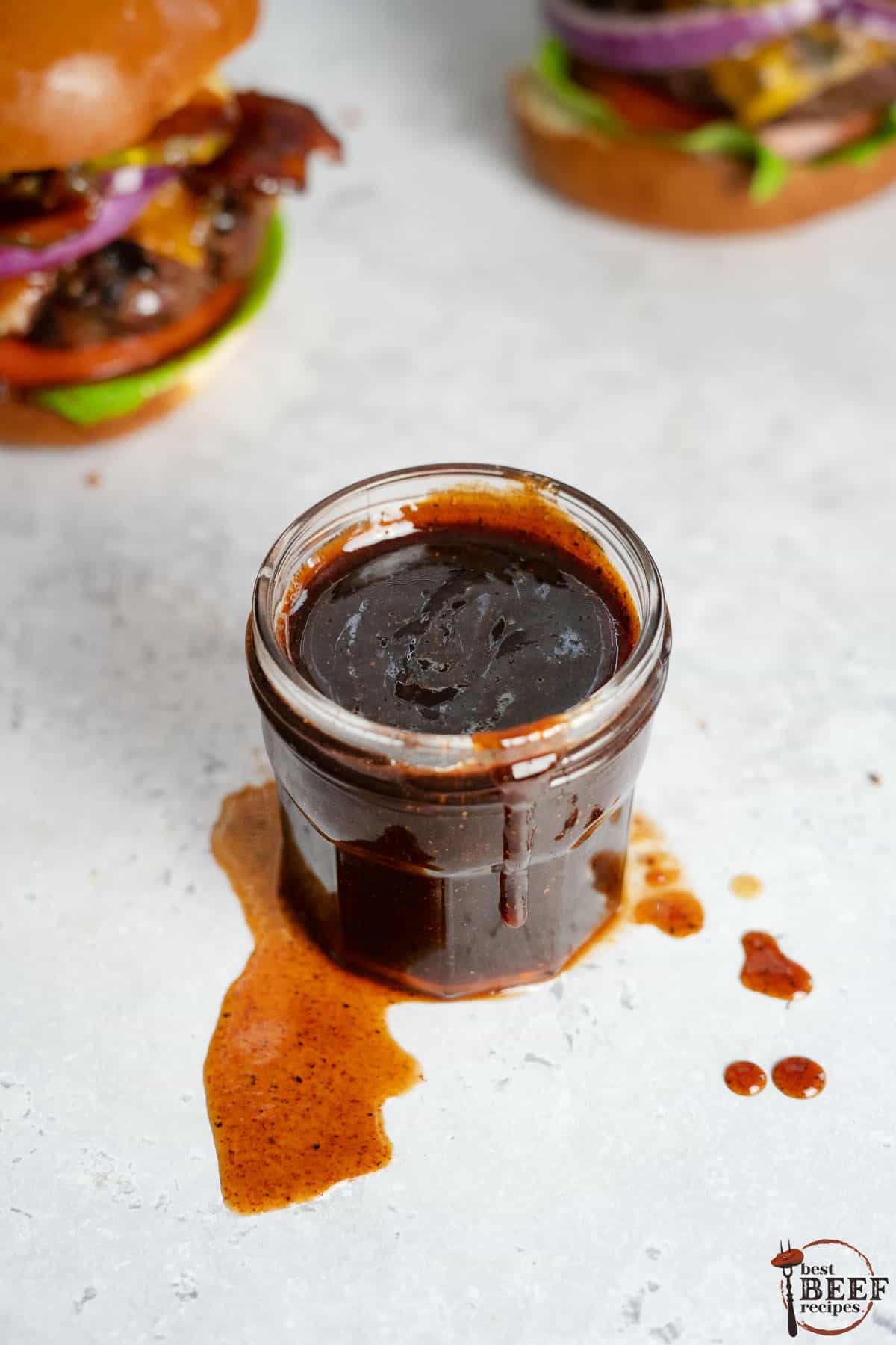 bbq sauce in a clear jar with burgers in the background