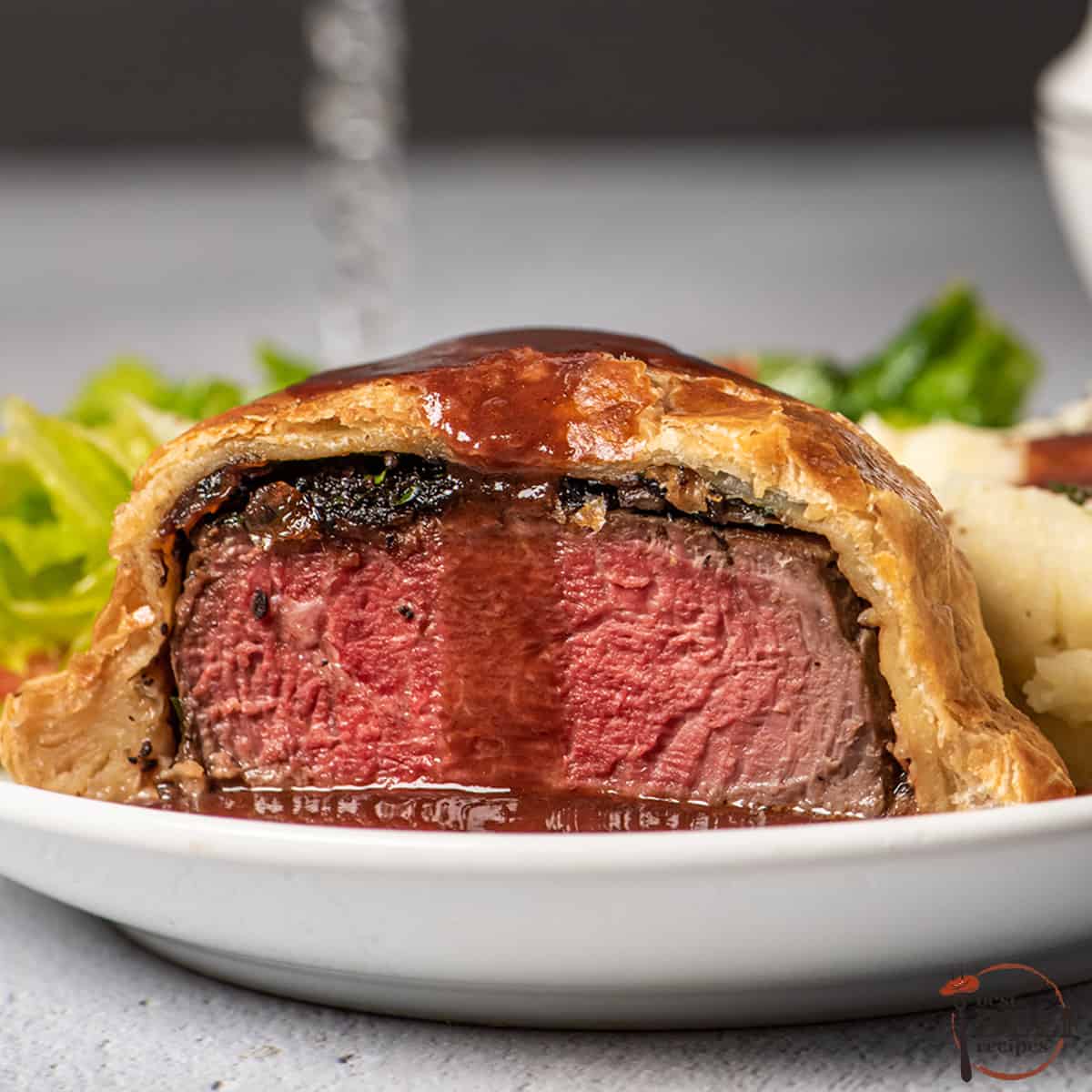 sliced beef wellington with espagnole sauce poured over top