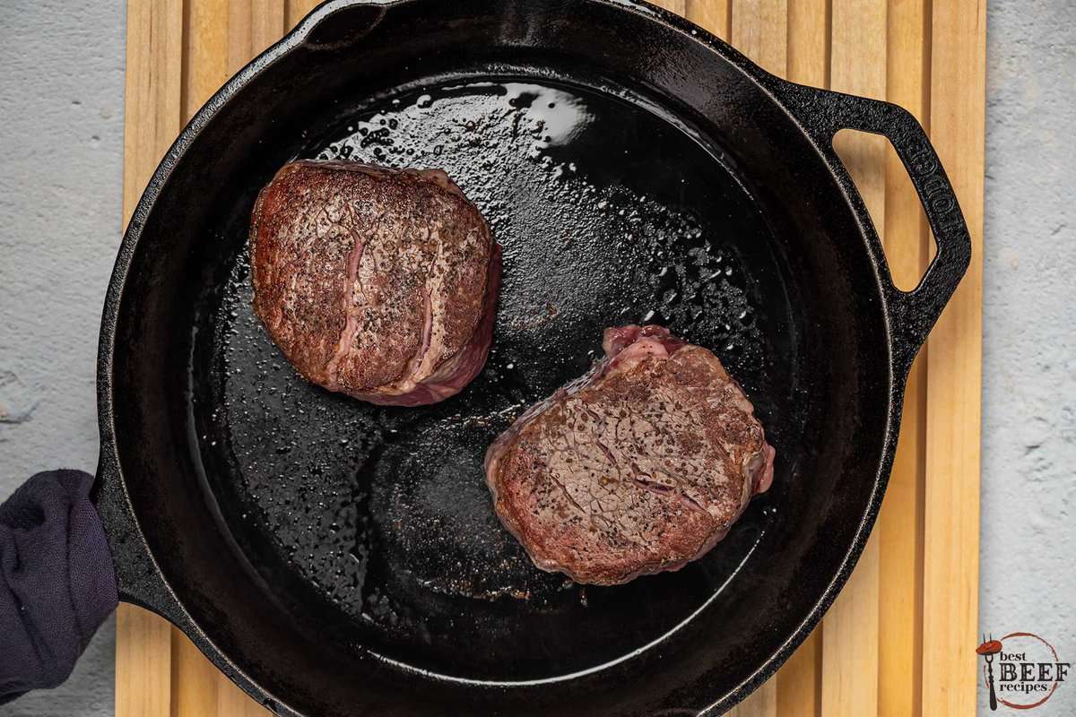 the steaks being seared on a cast iron pan