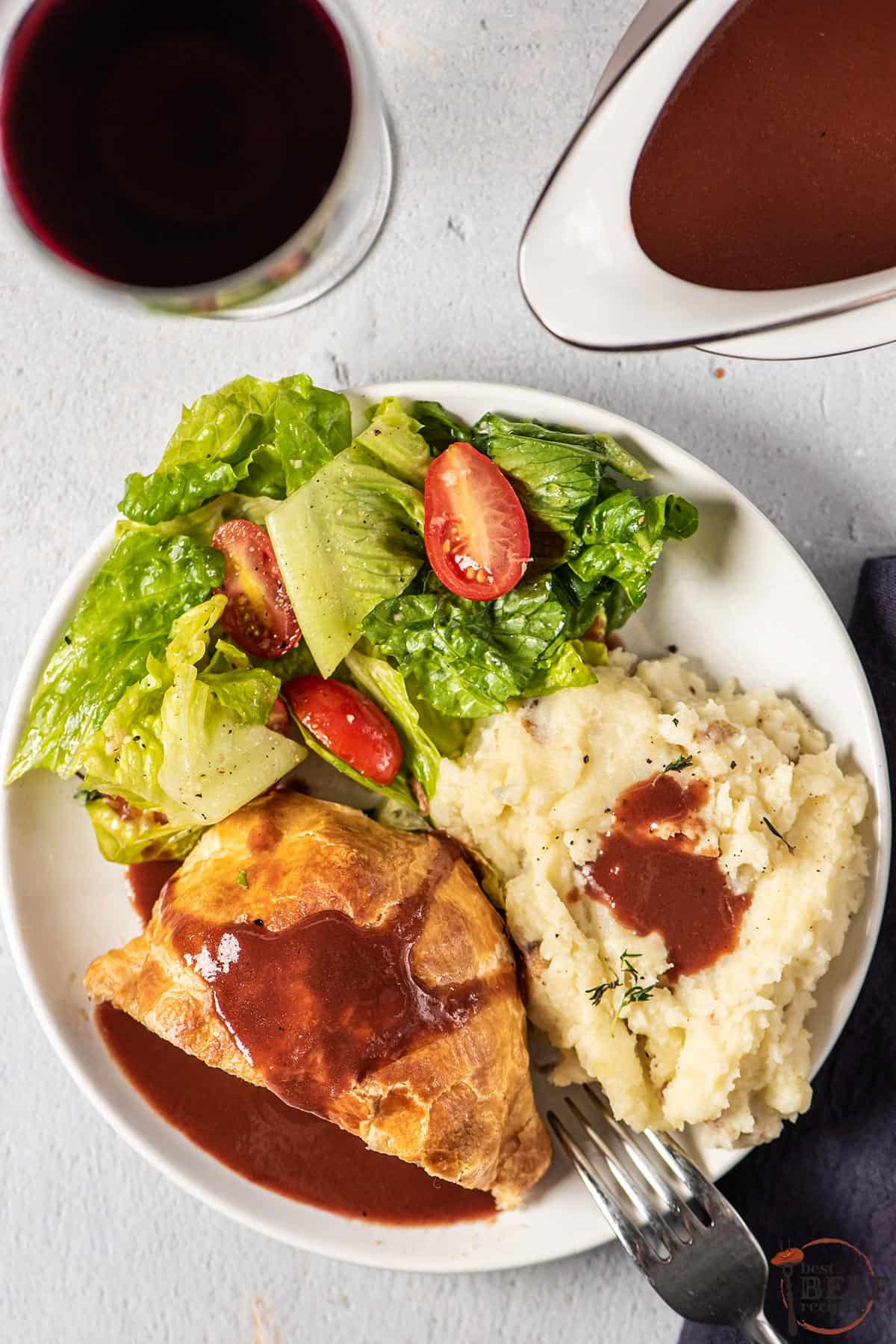 a dinner plate filled with mashed potatoes, salad, and beef wellington, topped with espagnole sauce