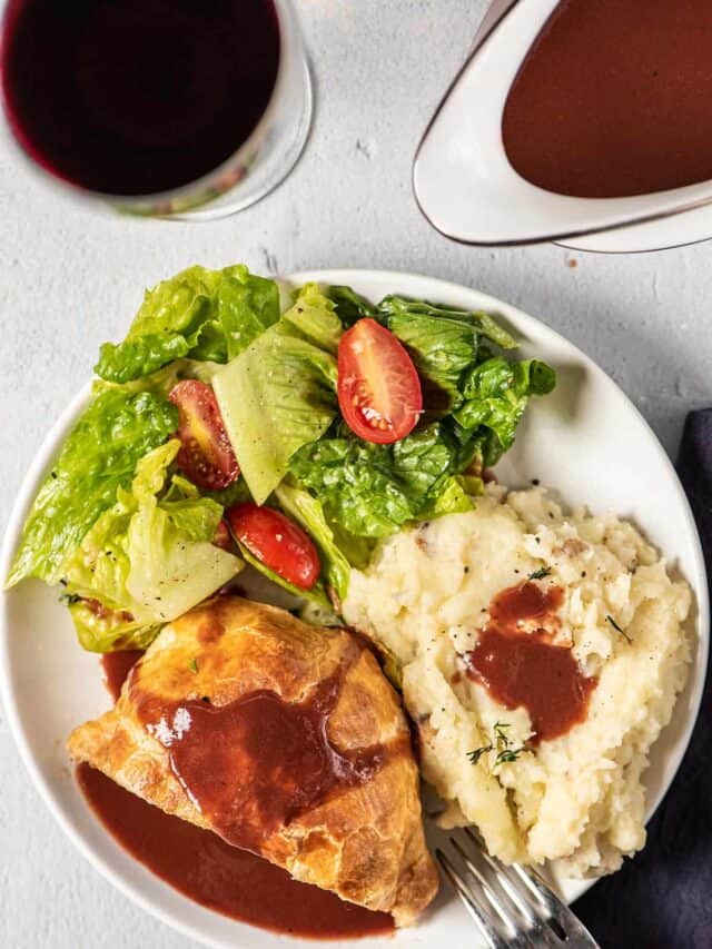 a dinner plate filled with mashed potatoes, salad, and beef wellington, topped with espagnole sauce
