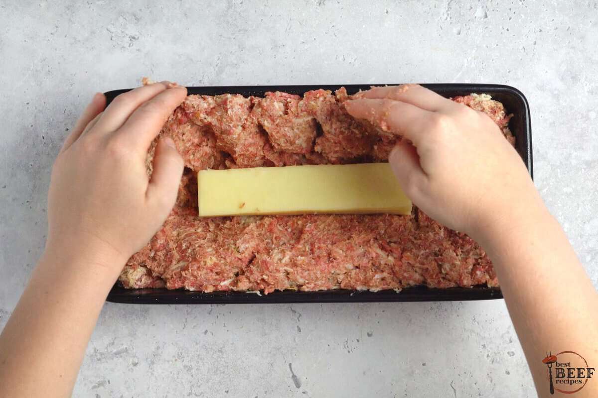 adding a stick of mozzarella cheese in the middle of the meatloaf beef inside of a loaf pan