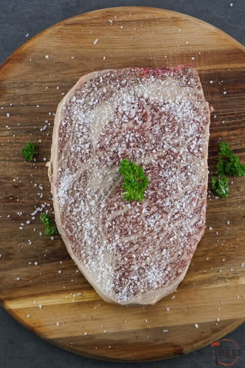 wagyu steak seasoned with salt and herbs on a board