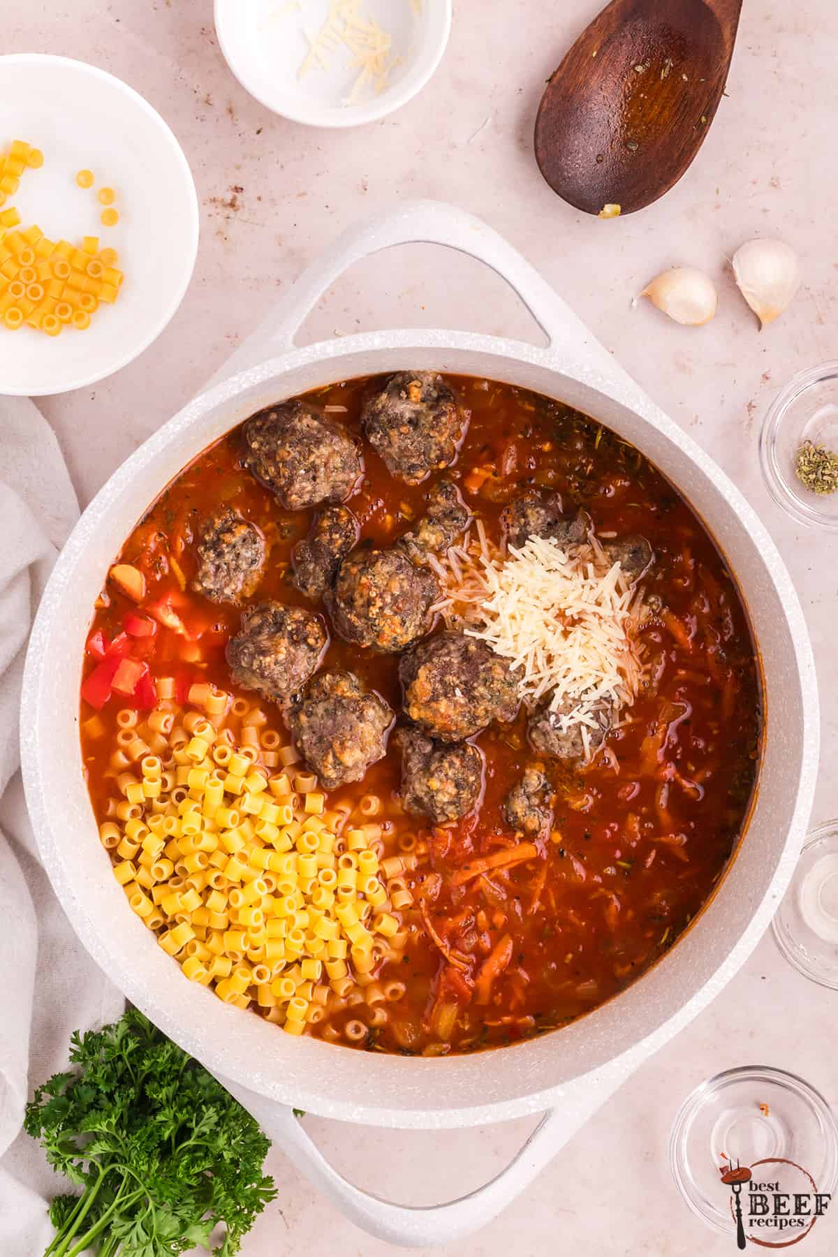 adding meatballs, pasta, and parmesan to soup in a pot