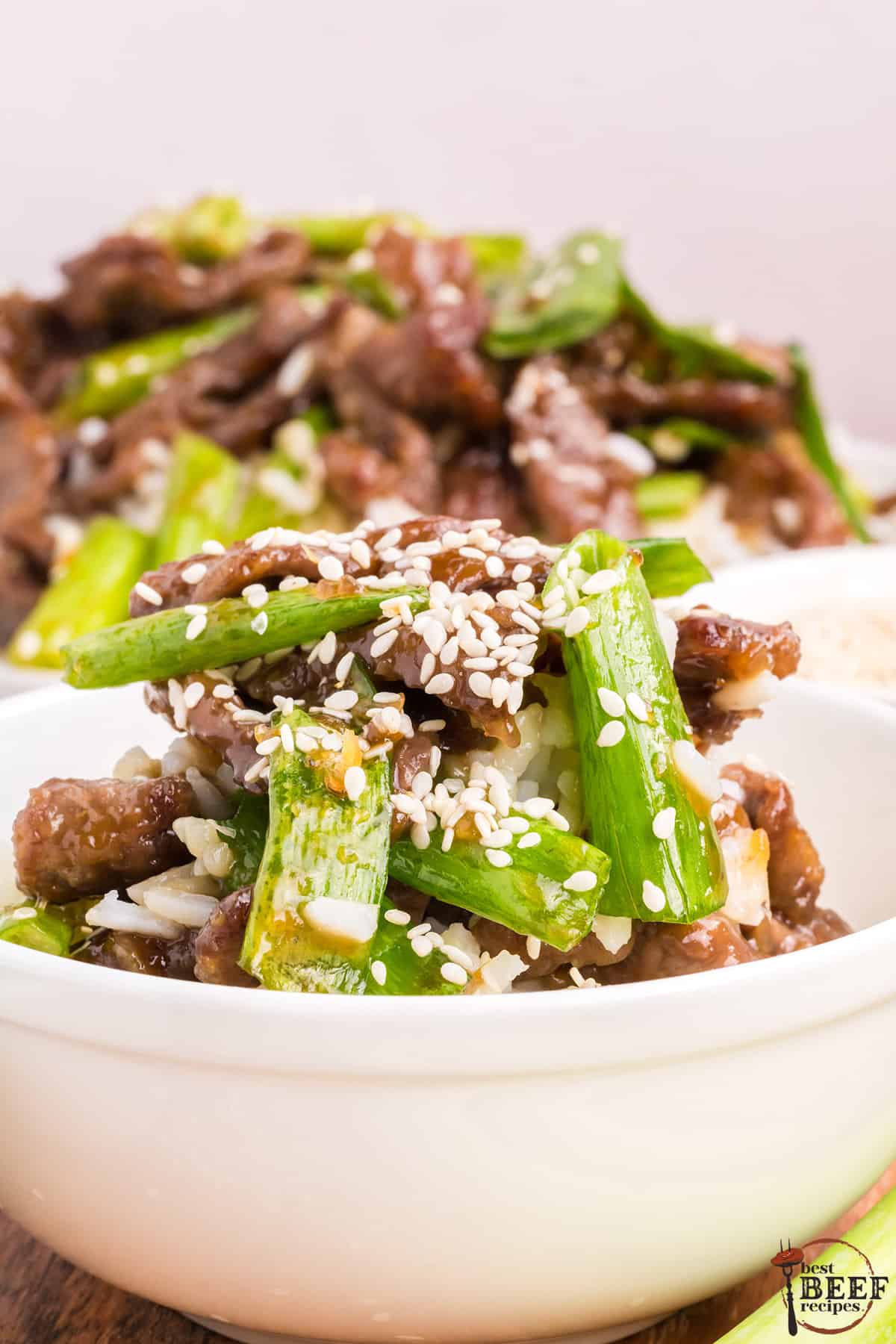 mongolian beef in a white bowl with green onions and sesame seeds