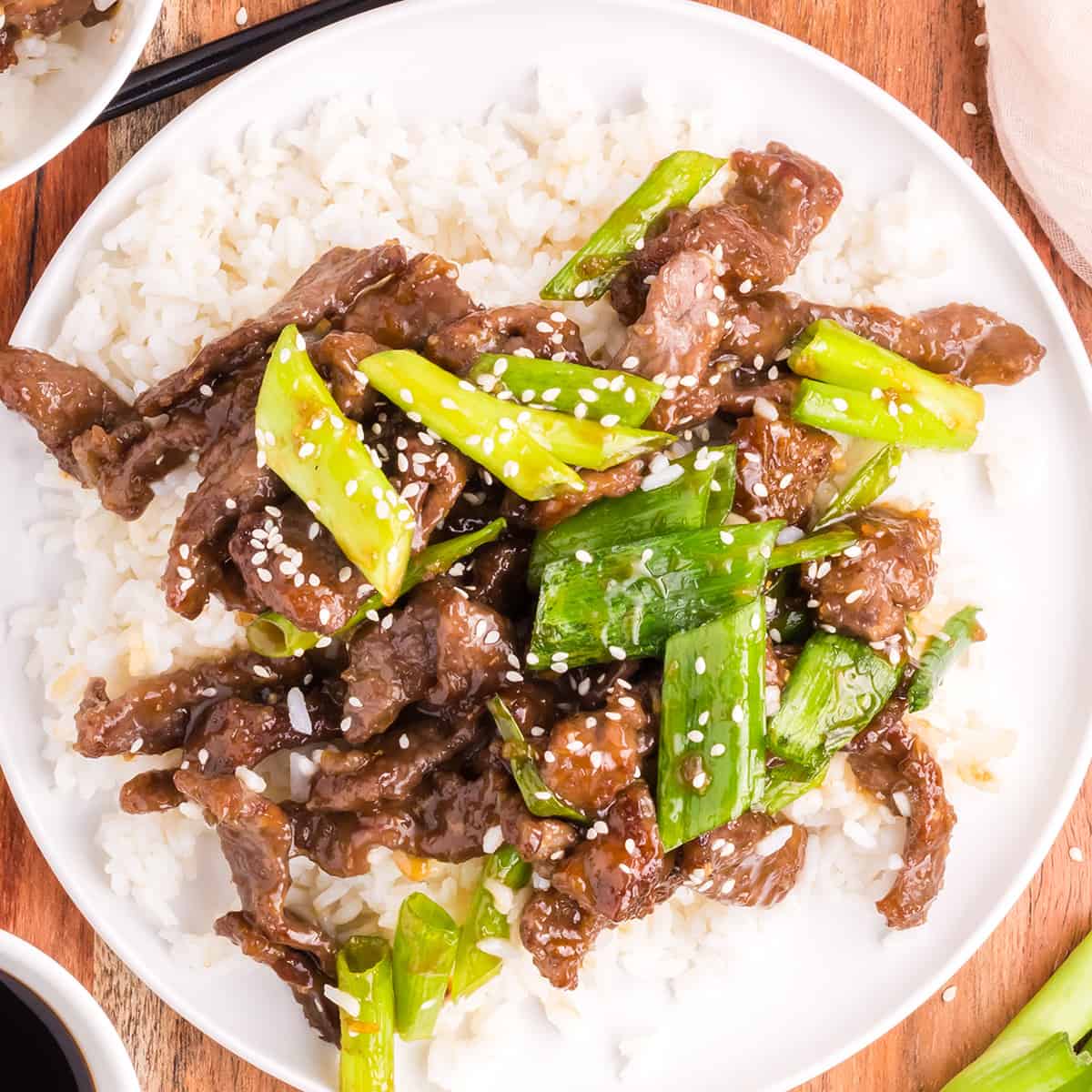 mongolian beef over rice with sliced green onion stalks and sesame seeds