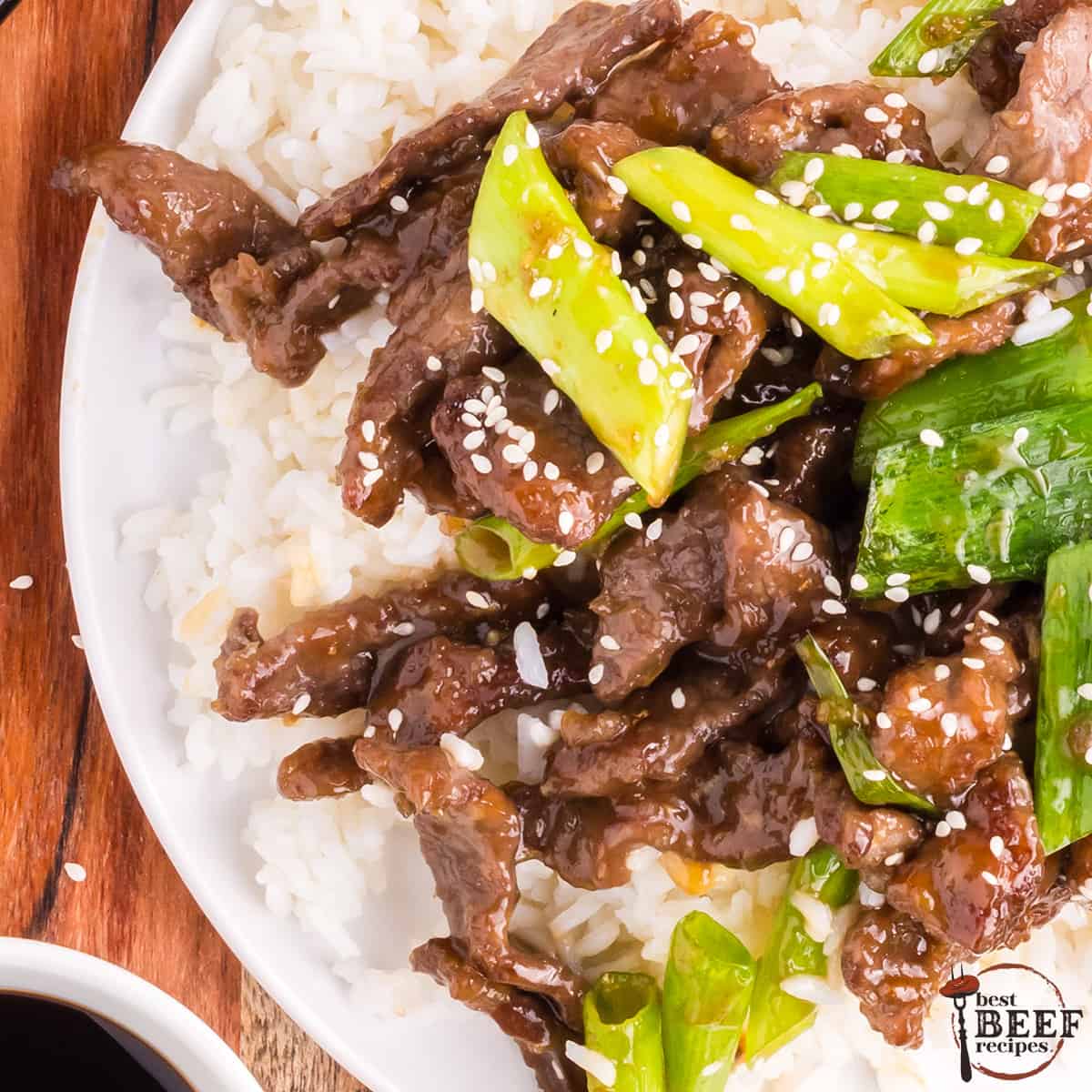 mongolian beef over rice in a bowl with green onions and sesame seeds