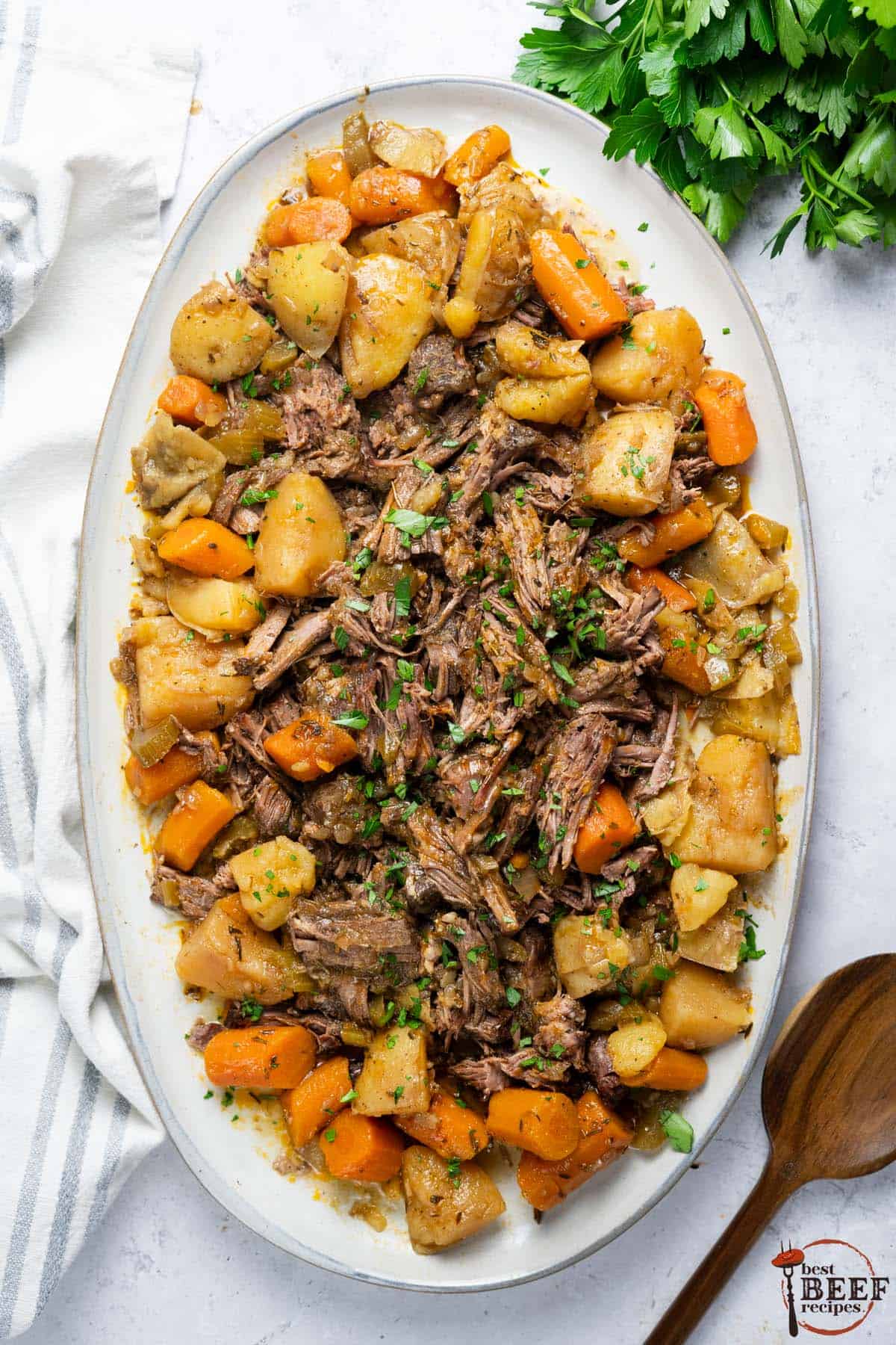 shredded slow cooker roast beef on a platter with carrots and potatoes