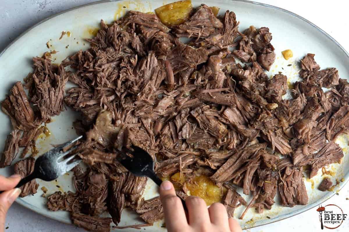 shredding roast beef with two forks on a platter