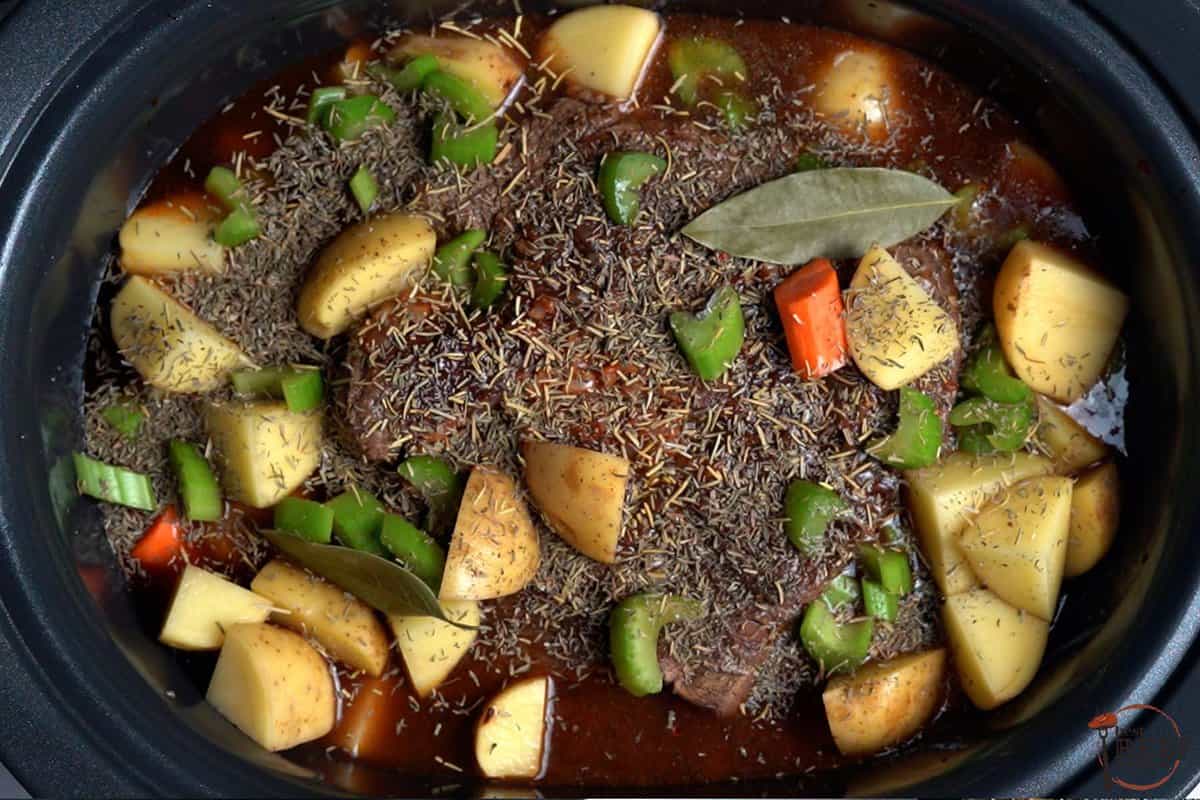 adding seasonings and vegetables to slow cooker with beef