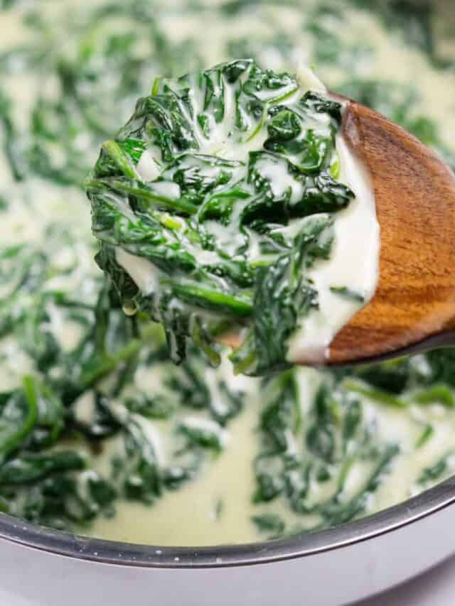 a wooden spoon full of creamed spinach over a pot of creamed spinach