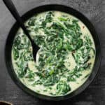 a black bowl filled with creamed spinach with a spoon