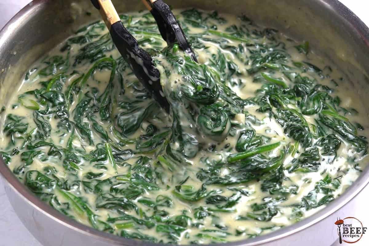 tongs mixing creamed spinach in a pot