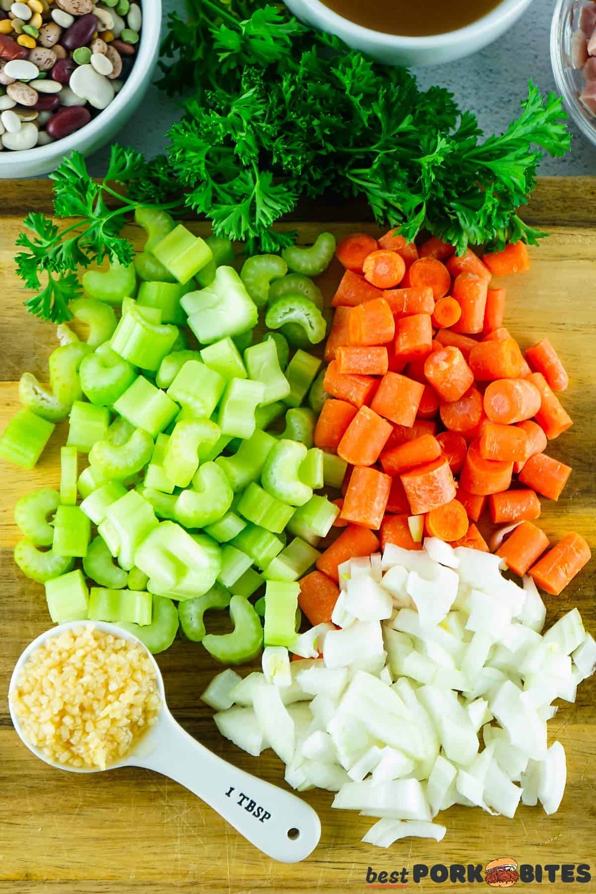 chopped celery, carrots, onions and garlic on a cutting board with parsley and beans