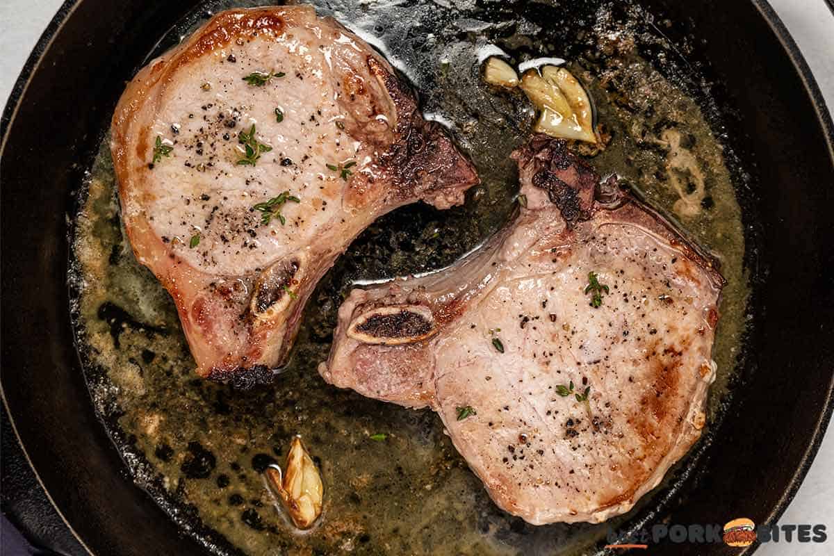 cooked pork chops in the skillet with melted butter, garlic, and thyme sprig