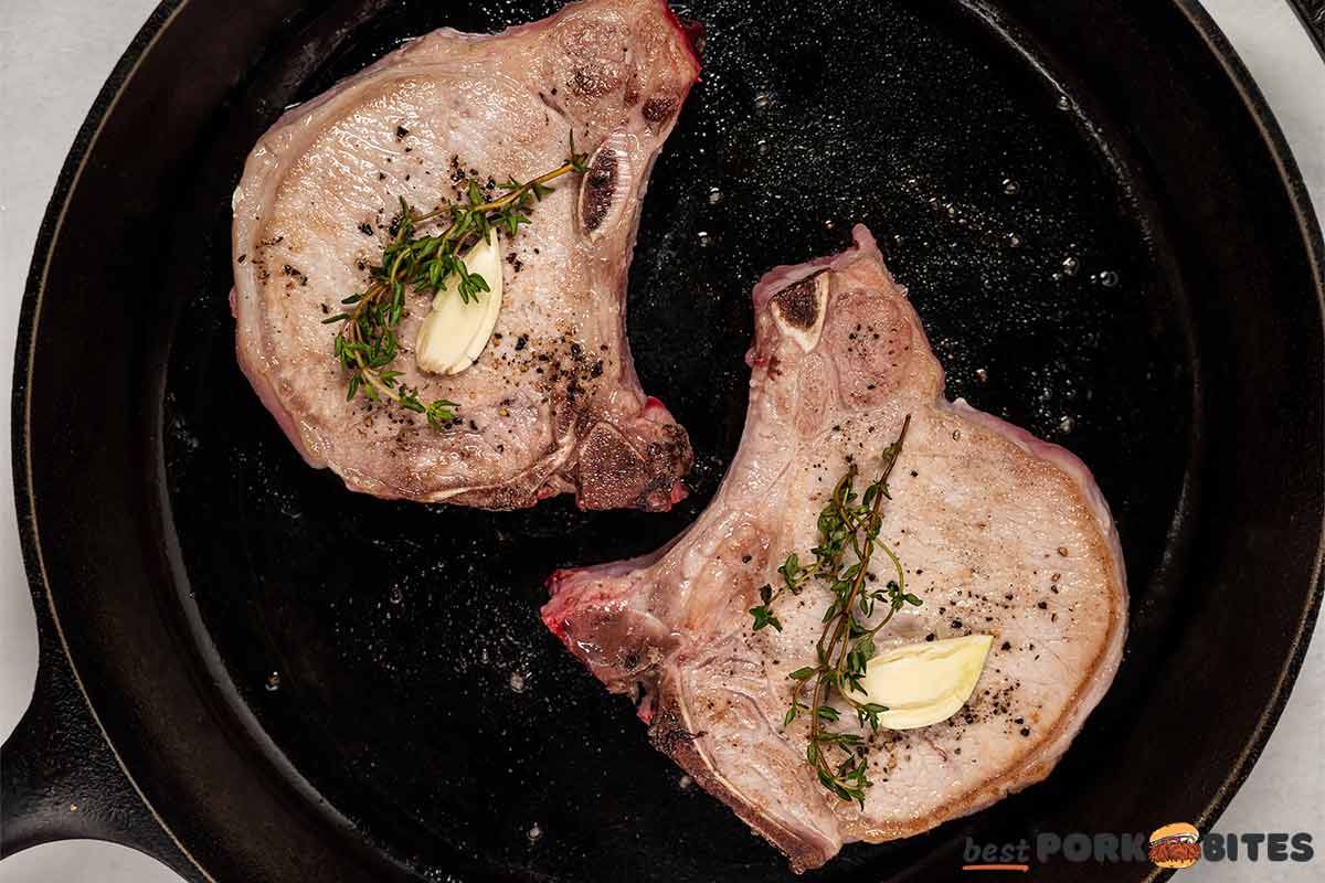cooked pork chops in a black skillet with thyme and garlic on top