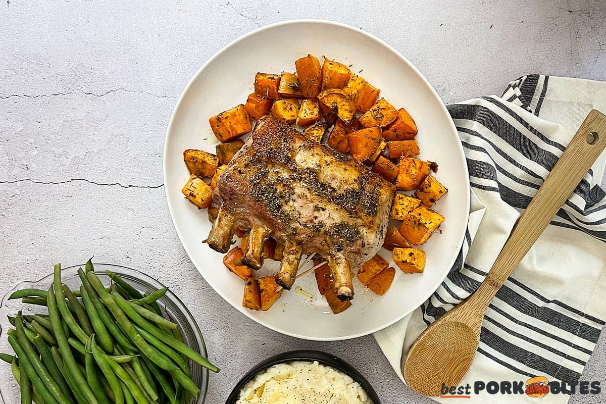 pork rib roast resting on a white plate with sweet potatoes