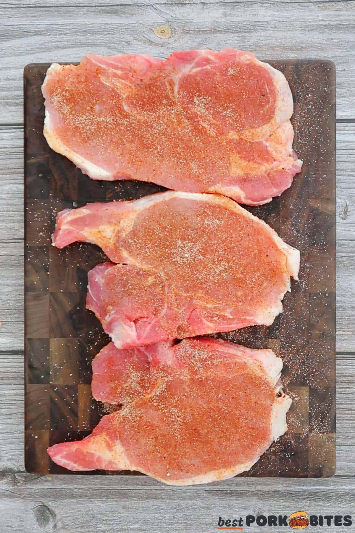 seasoning 3 pork chops on a cutting board