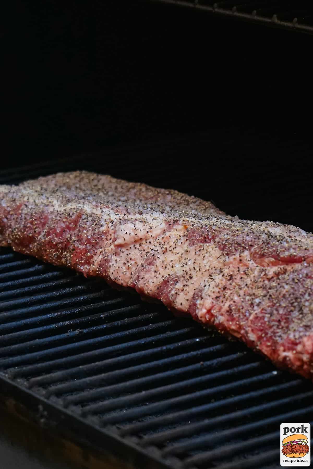 raw ribs seasoned and placed on a smoker