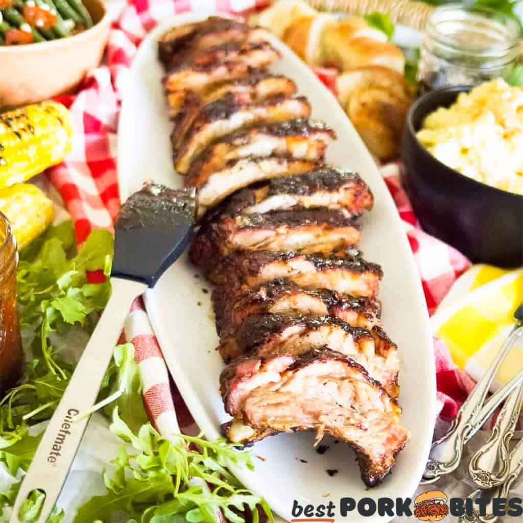 a rack of sliced pork ribs after being cooked on a serving platter with lettuce, corn, bread, potatoes and cutlery