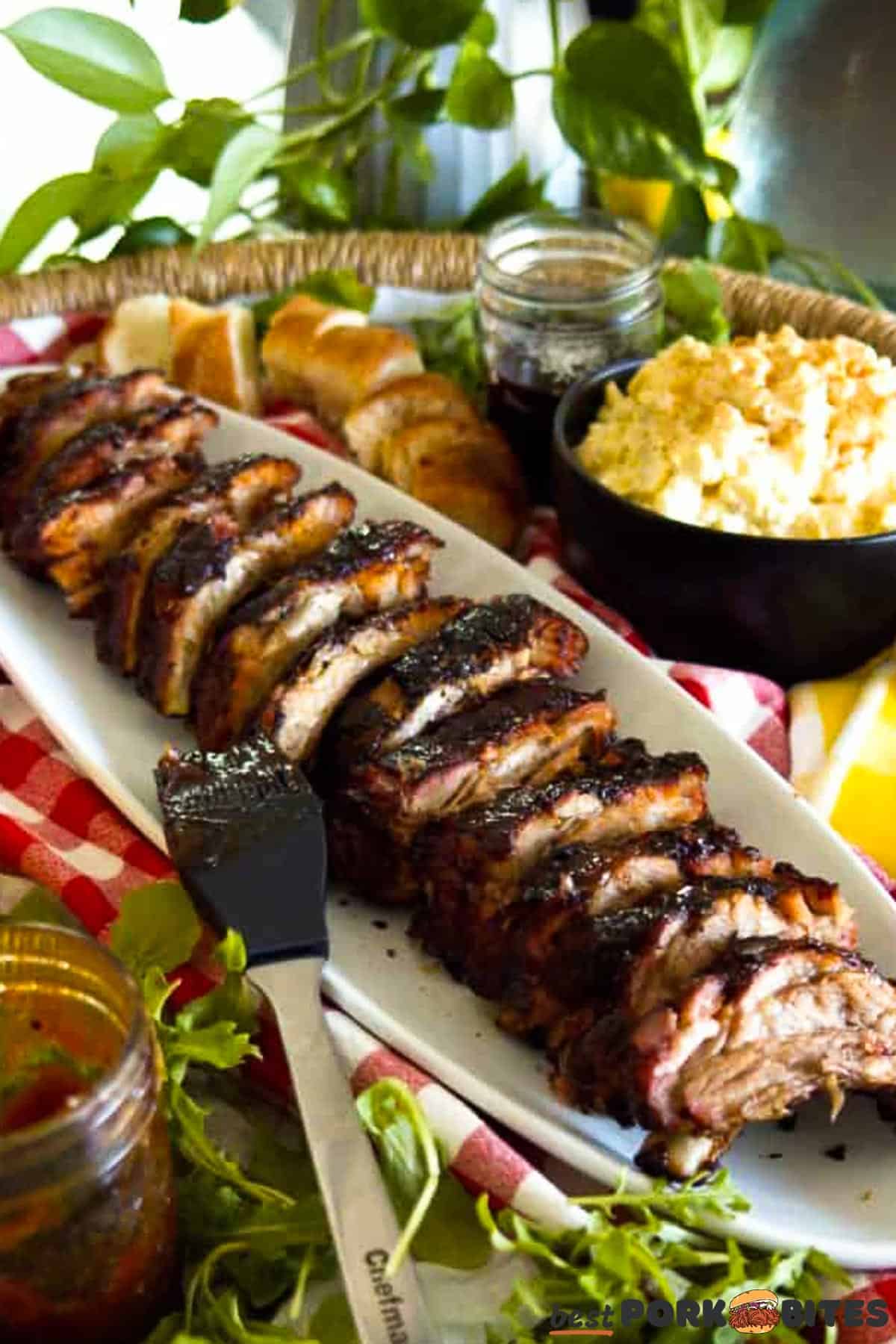a white platter of sliced ribs with sauce, bread, lettuce, and potatoes