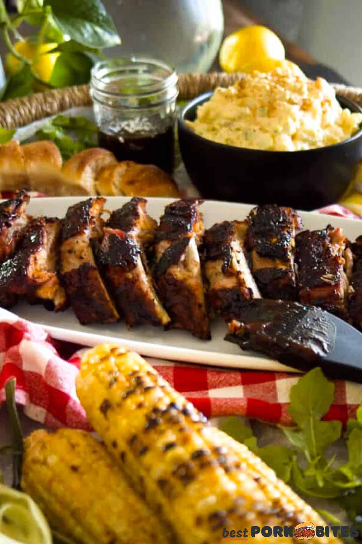 a platter of baby back ribs with a bowl of potatoes, a dish of sauce, and corn