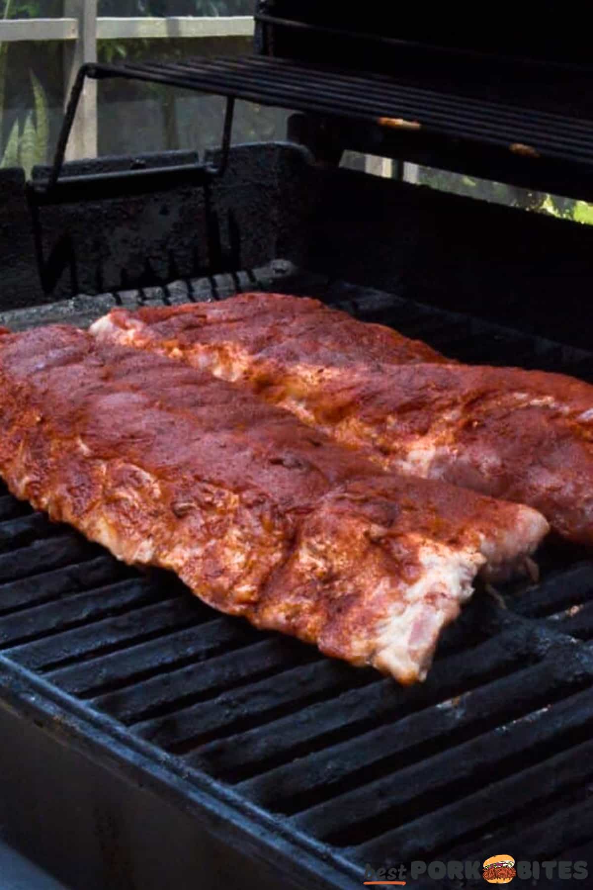 two racks of baby back ribs on a grill with BBQ sauce
