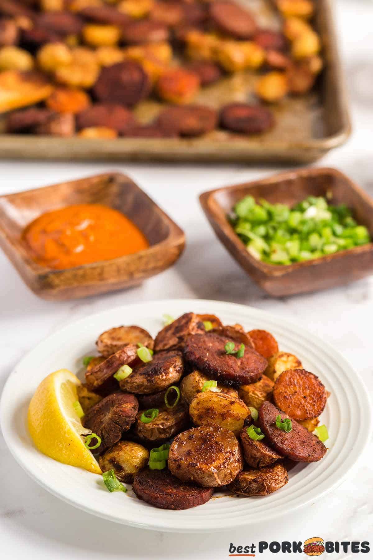 a white dish of potatoes with chorizo with a background of a dish of peri peri, a dish of green onions, and a sheet pan with more potatoes and chorizo