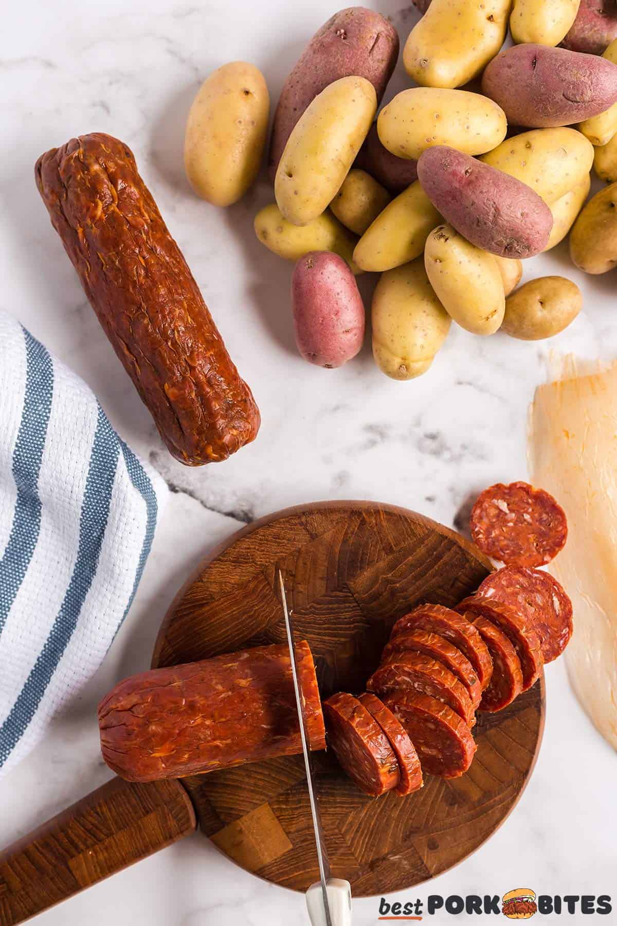 chorizo logs being sliced on a cutting board next to potatoes