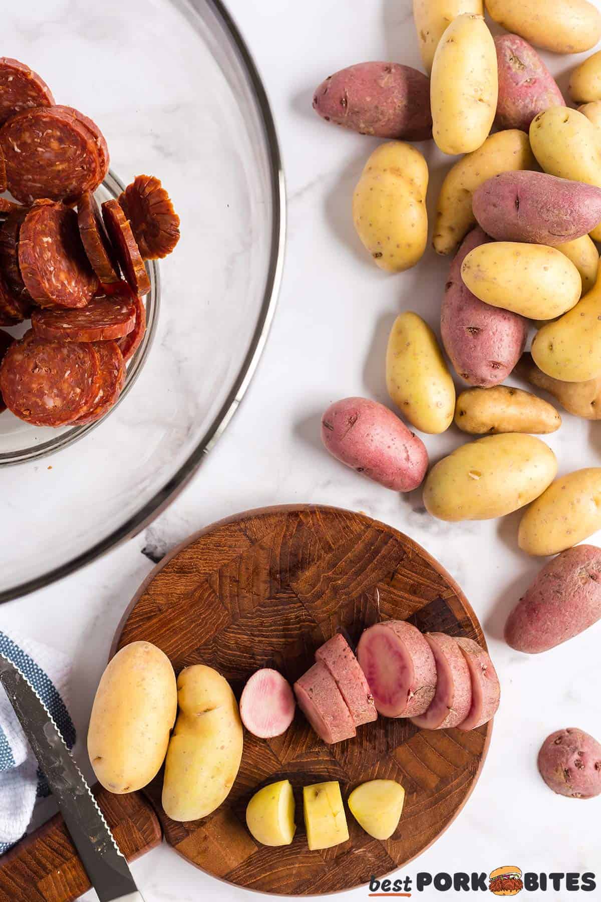 fingerling potatoes being sliced on a cutting board next to sliced chorizo and more potatoes