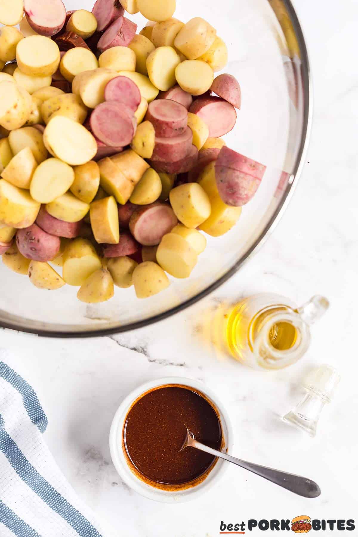 a glass bowl filled with sliced potatoes with chorizo next to a dish of seasoning and olive oil