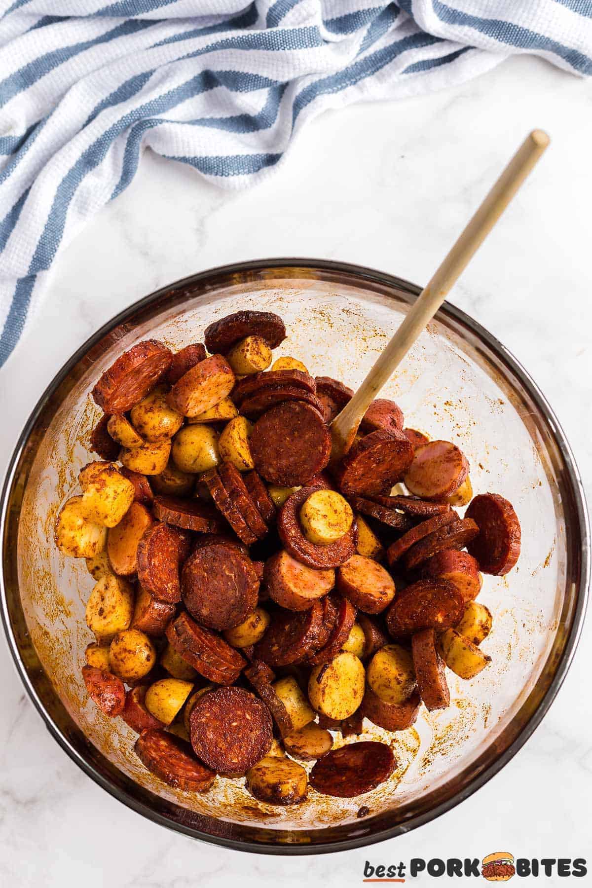 a mixing bowl with potatoes and chorizo coated in seasoning
