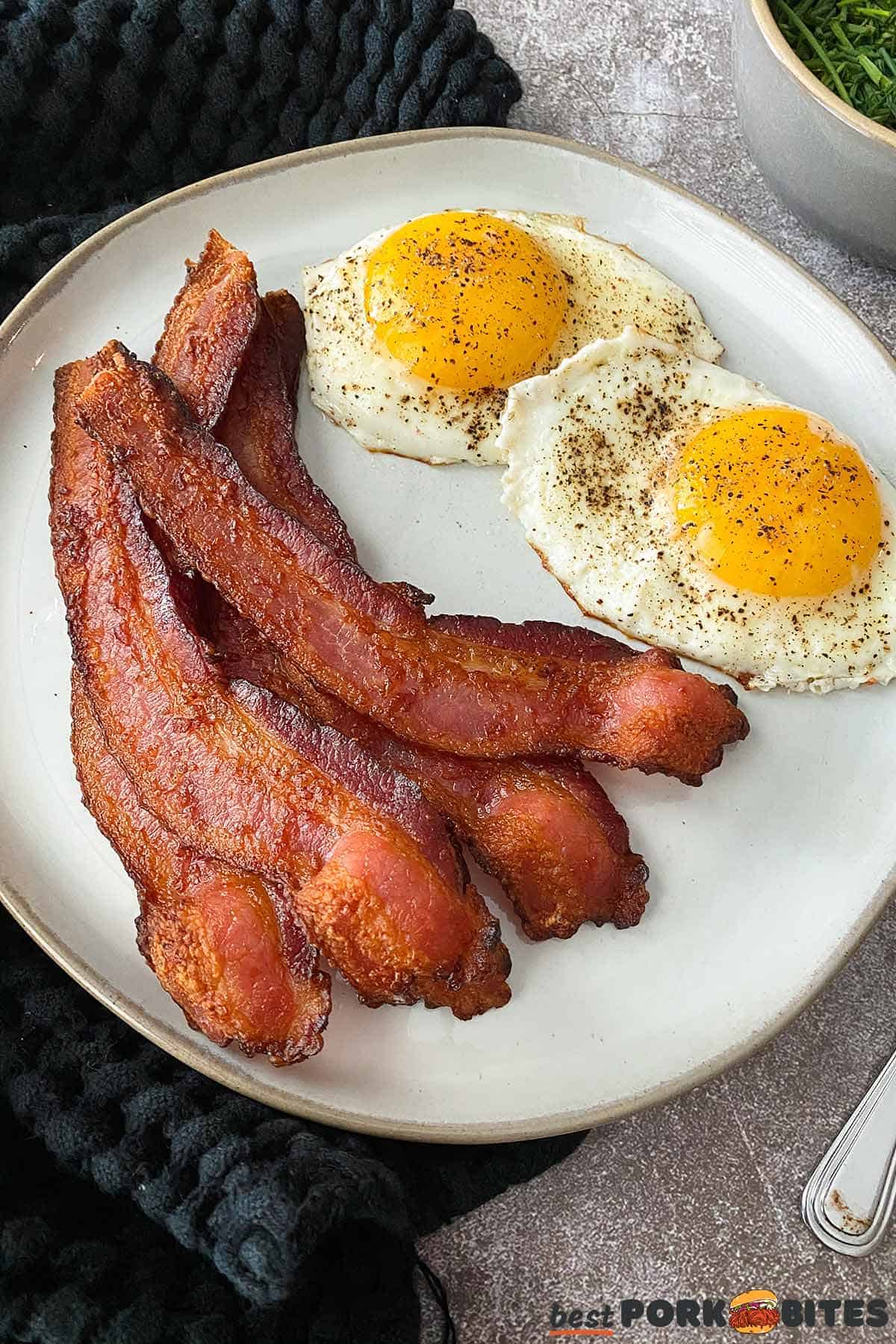 air fried bacon on a grey plate with over easy eggs next to it