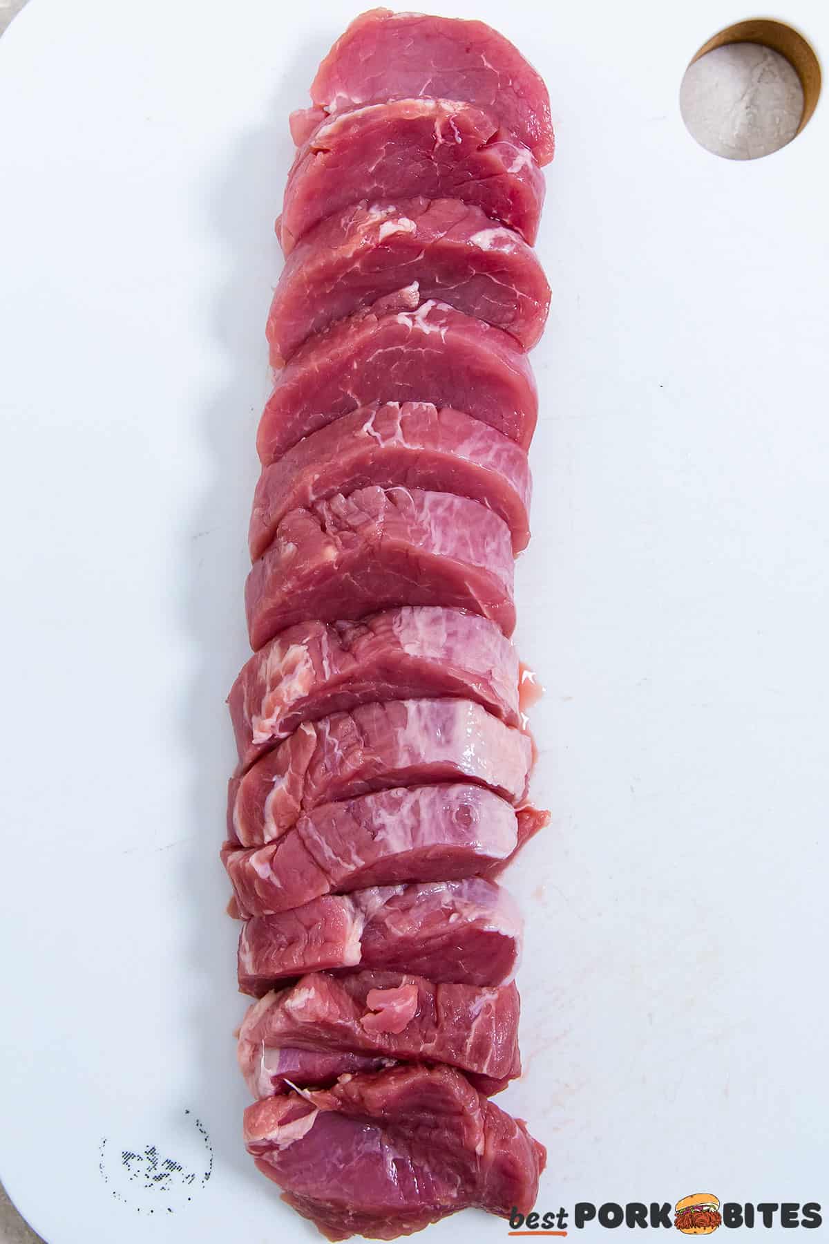 Sliced raw pork tenderloin on a white cutting board