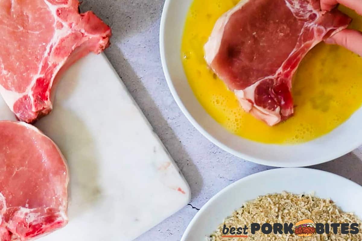 a raw pork chop being dipped in egg next to more pork chops