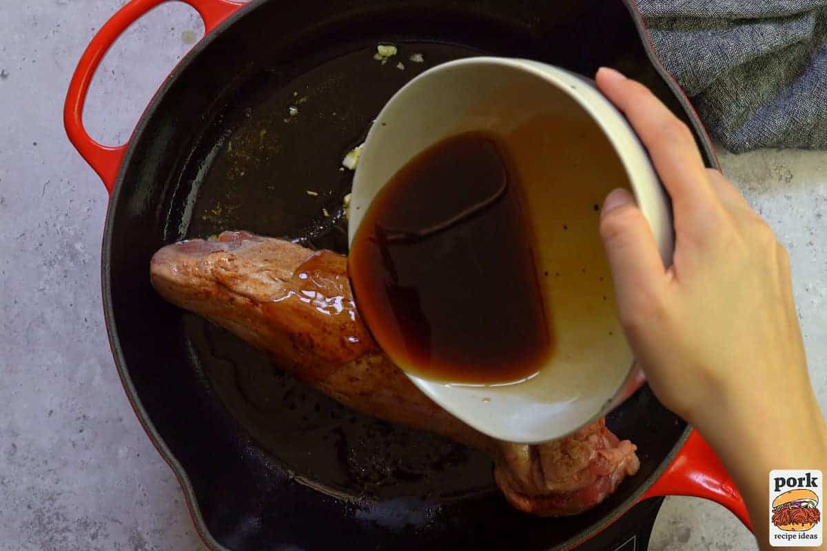 pouring sauce over pork tenderloin in pan