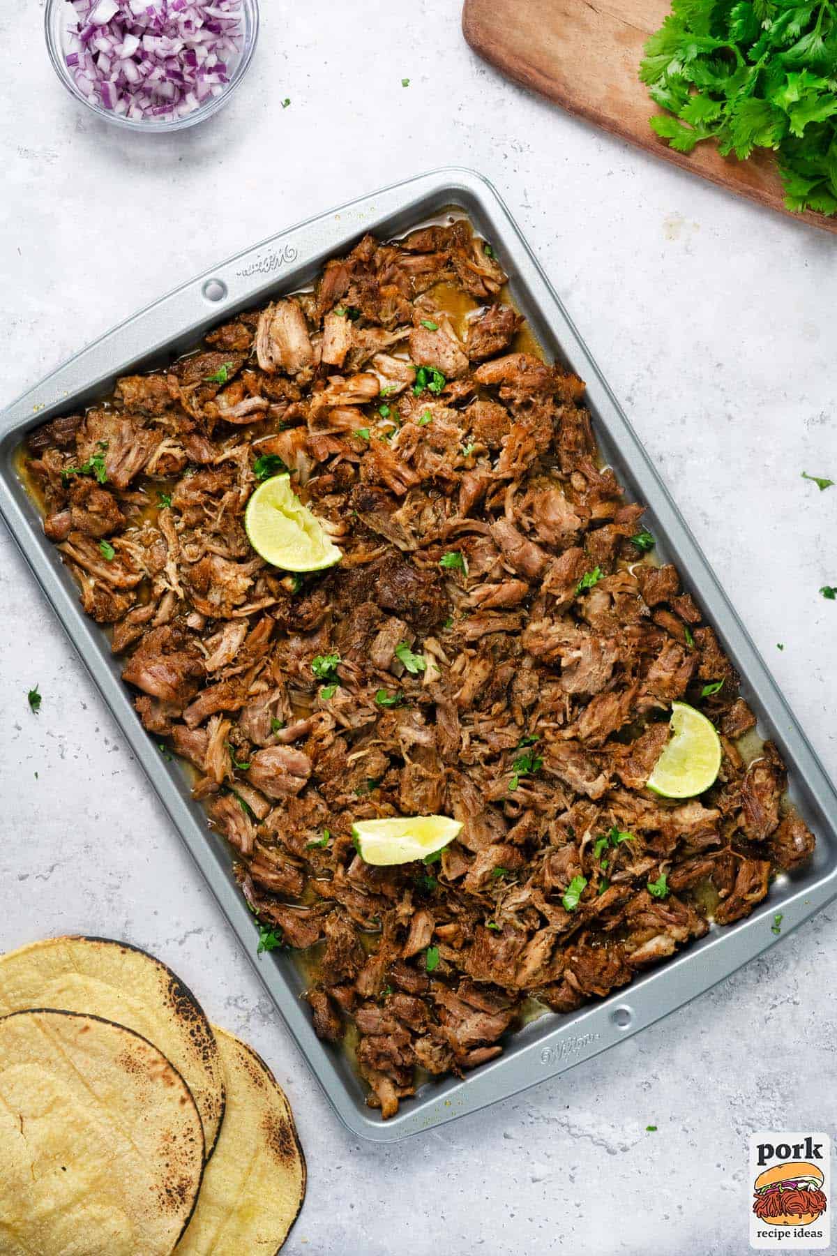 a sheet pan of carnitas with extra red onion, cilantro, and tortillas