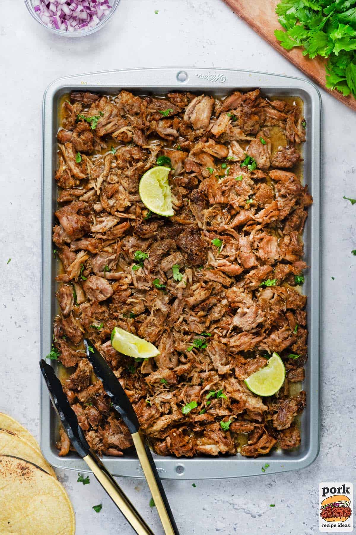 a sheet pan filled with shredded carnitas, lime wedges, and cilantro