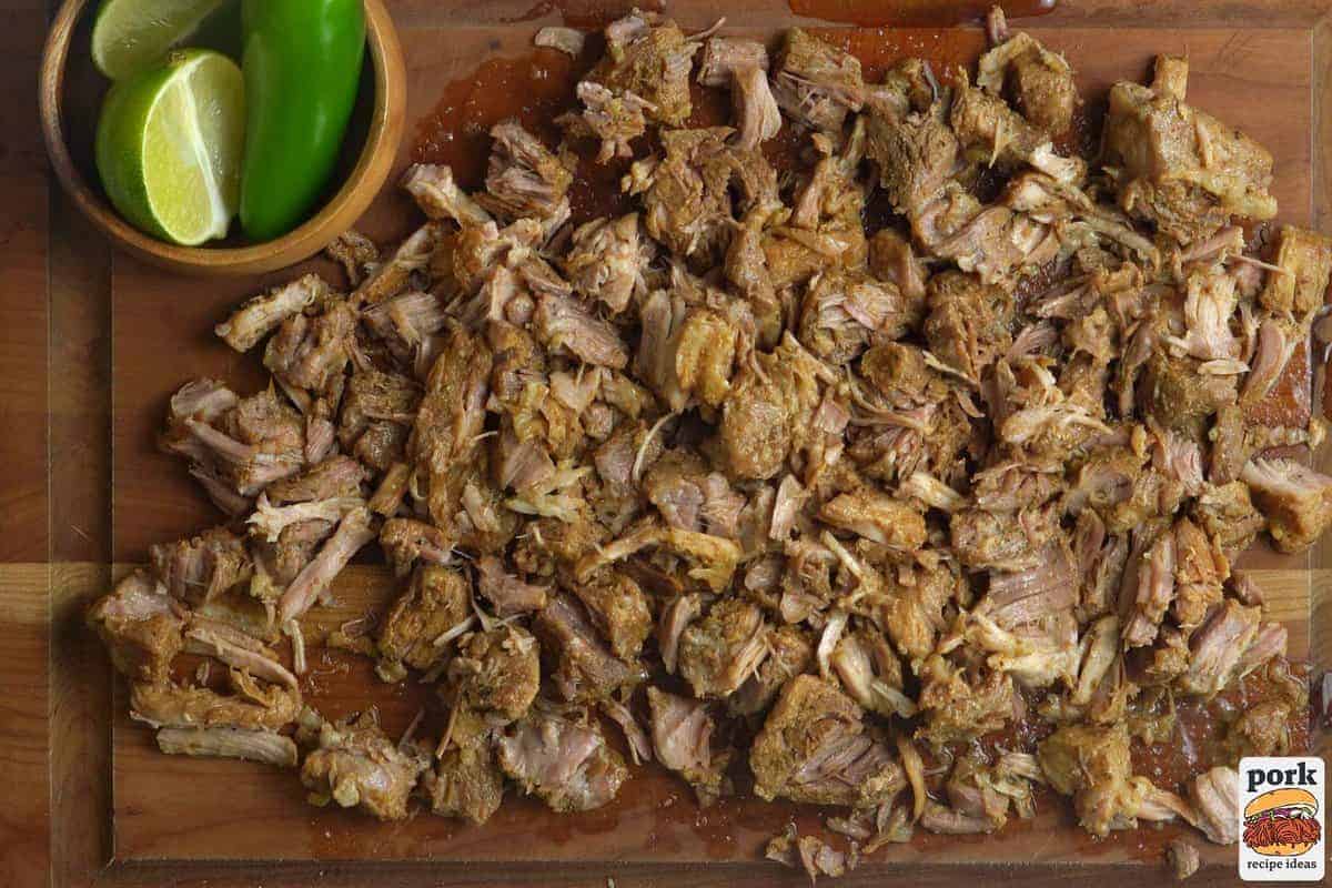 cooked carnitas removed from the pot and shredded on a cutting board