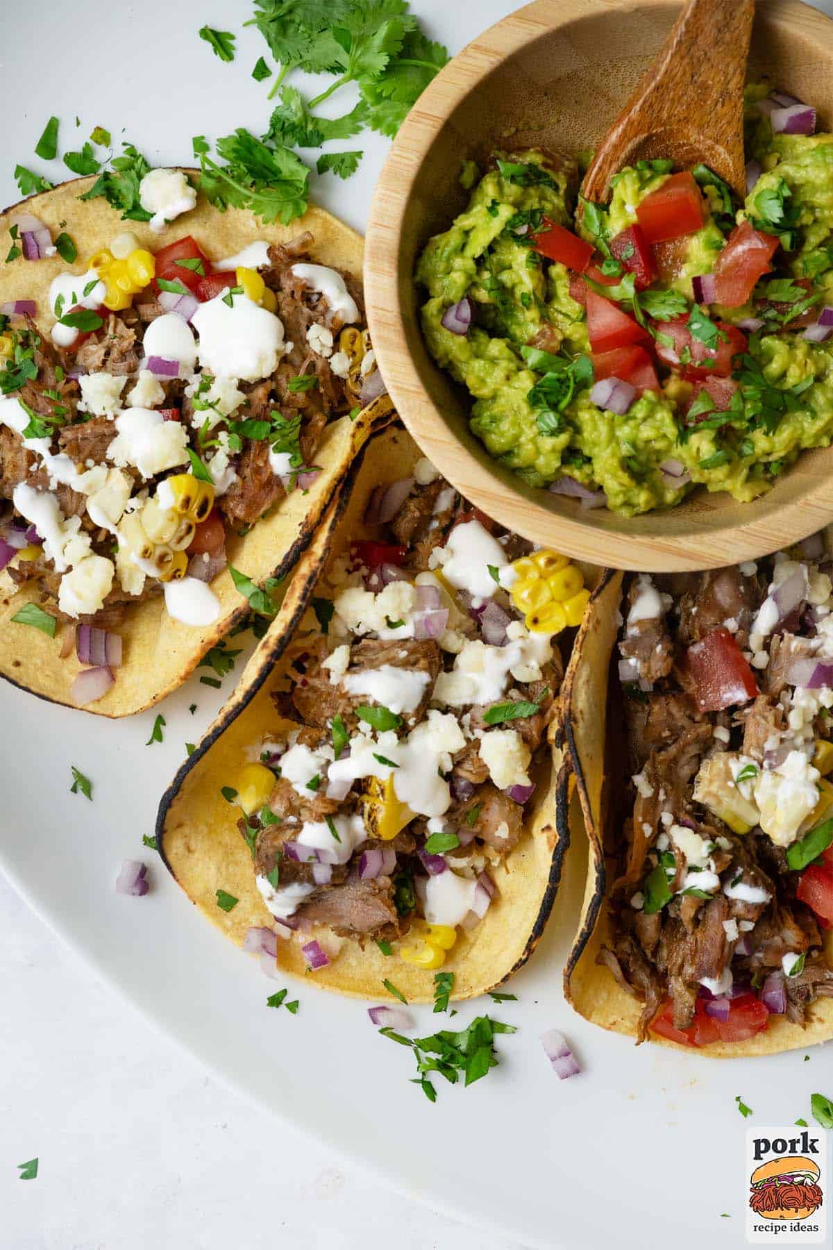 a closeup of three carnitas tacos and a bowl of fresh guacamole