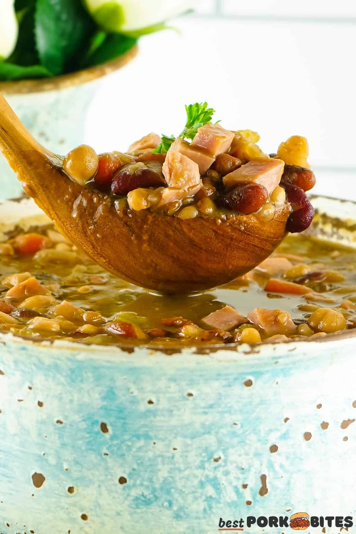 a wooden soup spoon full of soup over a blue pot of ham and bean soup